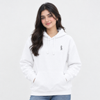 A woman with long dark hair wearing a white pullover hoodie with a small gray graphic on the left chest, paired with blue jeans, against a plain light gray background.